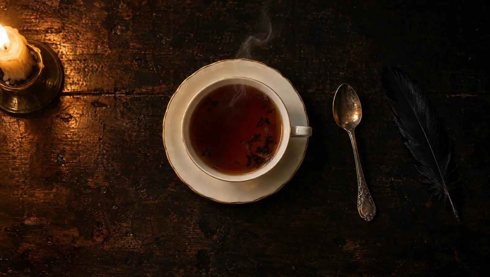 Teetasse von oben auf dunklem Holztisch, daneben Kerze, Löffel und Rabenfeder